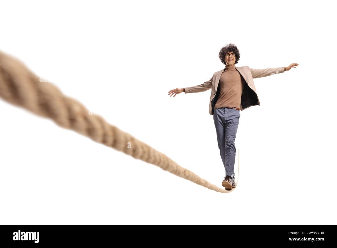 Excited young man with curly hair walking on a tightrope and smiling isolated on white background Stock Photo