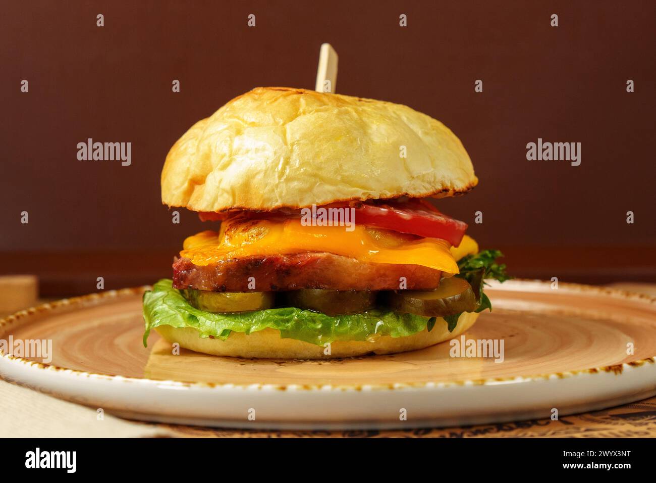 Cheeseburger topped with fresh lettuce and tomato on a sesame seed bun, ready to be enjoyed. Stock Photo