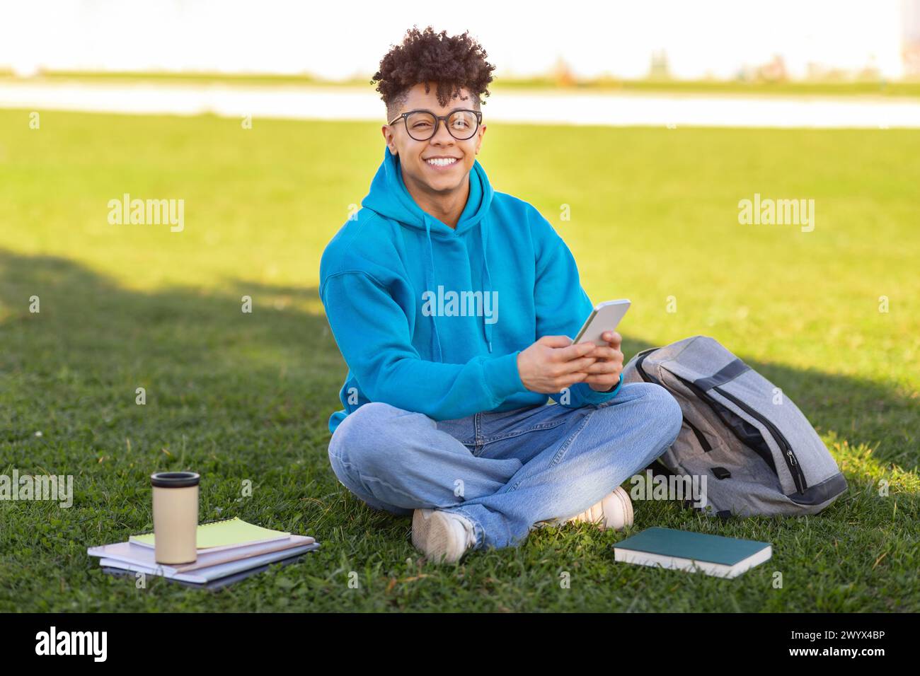 Student sitting on grass with smartphone, studying at park Stock Photo
