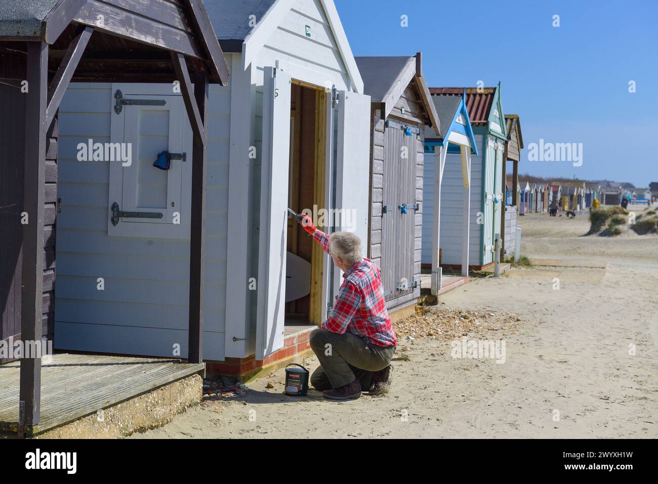 Man painting a beach hut  at West Wittering in Spring, preparing  it for the Summer season's use. Stock Photo