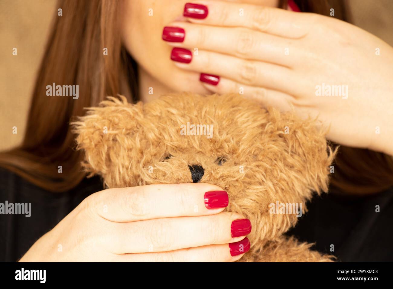 The girl covers her mouth and covers the mouth of a teddy bear, a secret , you can t tell Stock Photo