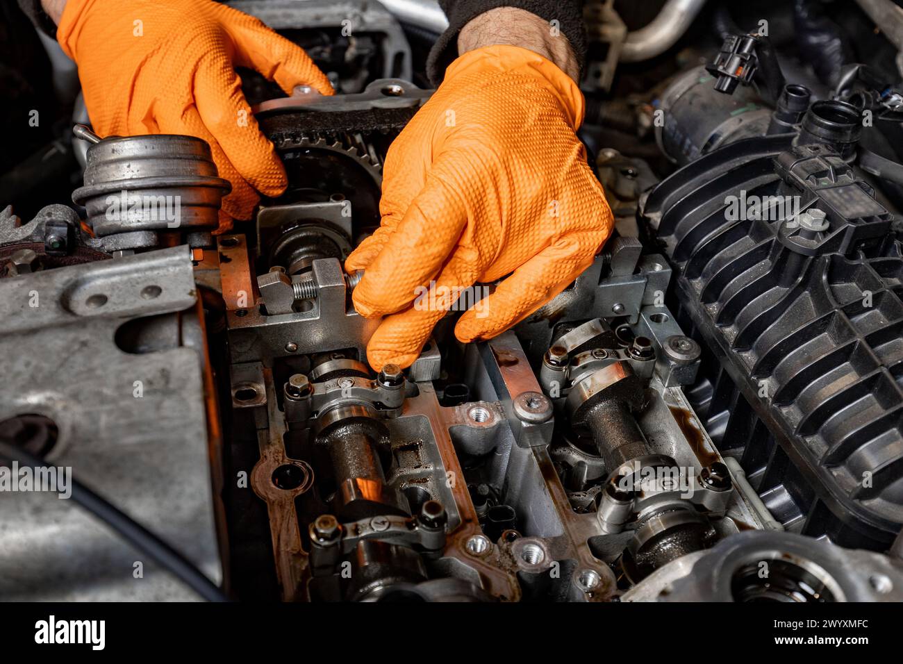 Detailed view of a car mechanic's hands, protected by orange gloves, as they attentively work on repairing an opened car engine in an auto service Stock Photo