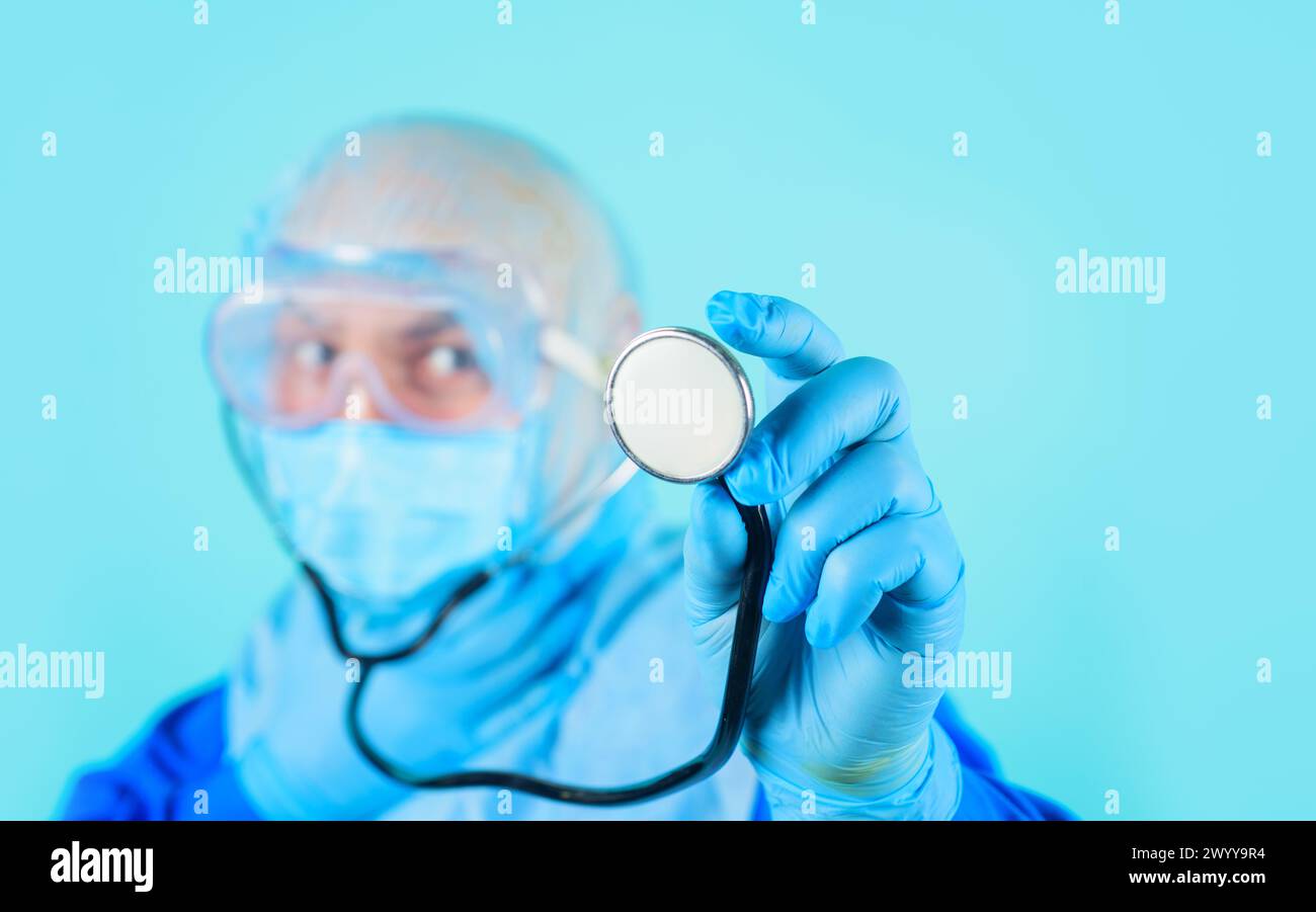 Closeup of doctor's hand in blue glove with stethoscope. Selective focus. Diagnostic instrument. Male doctor in medical uniform and surgical mask with Stock Photo