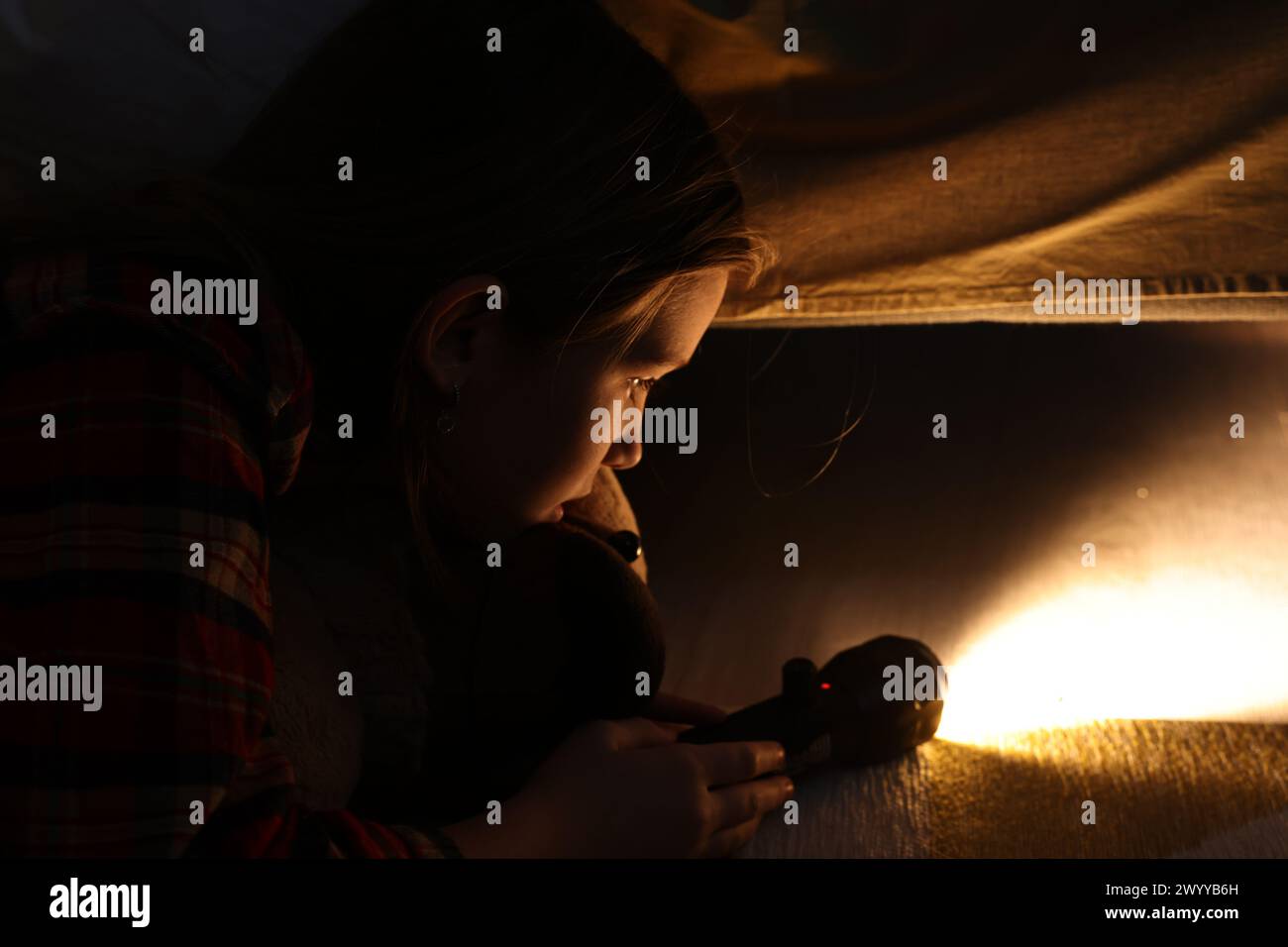 Little girl with flashlight looking for monster under bed at night Stock Photo