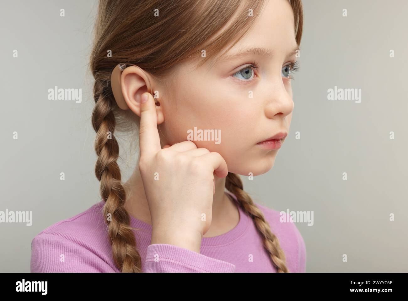 Little girl with hearing aid on grey background, closeup Stock Photo