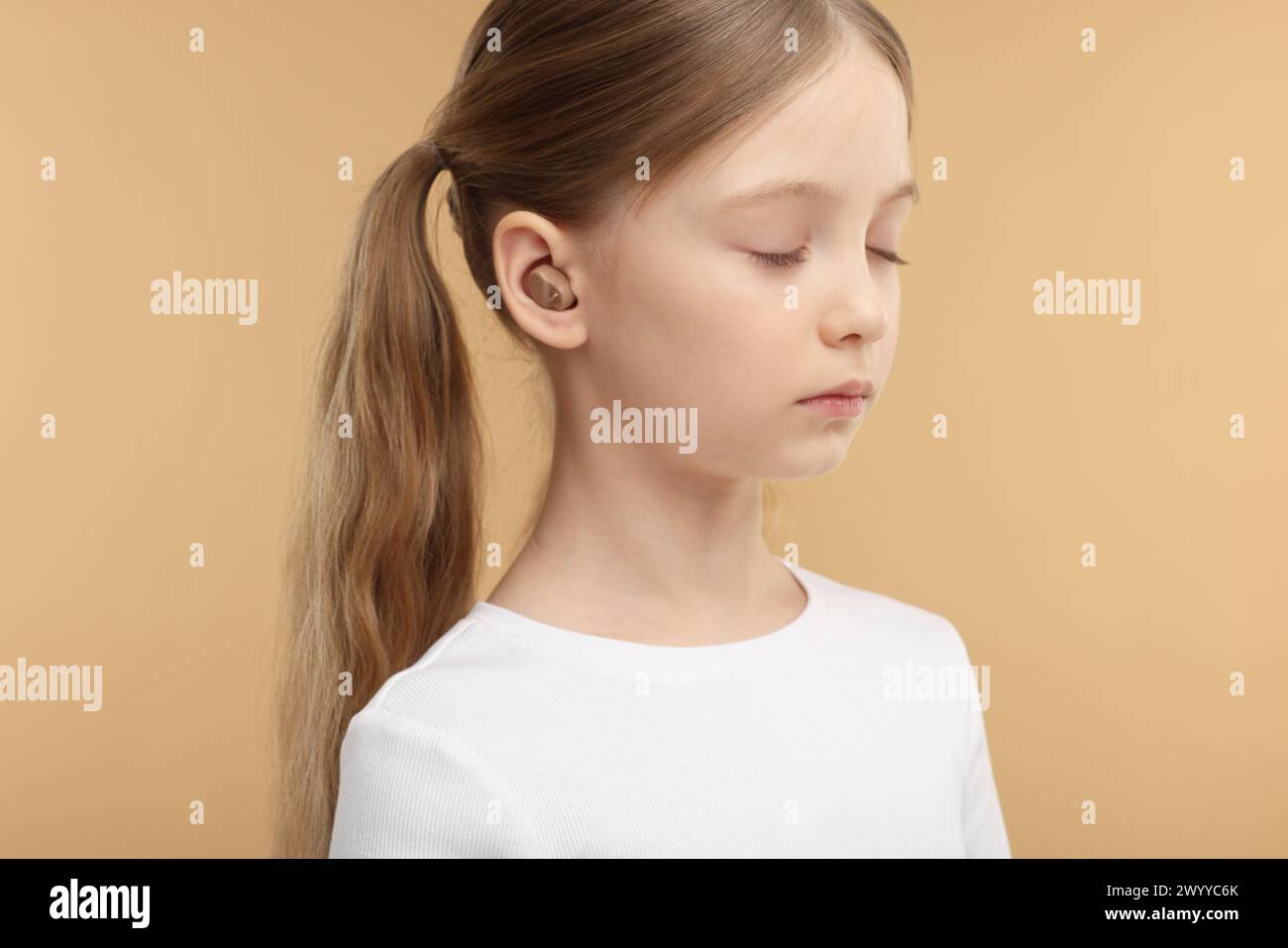 Little girl with hearing aid on pale brown background Stock Photo