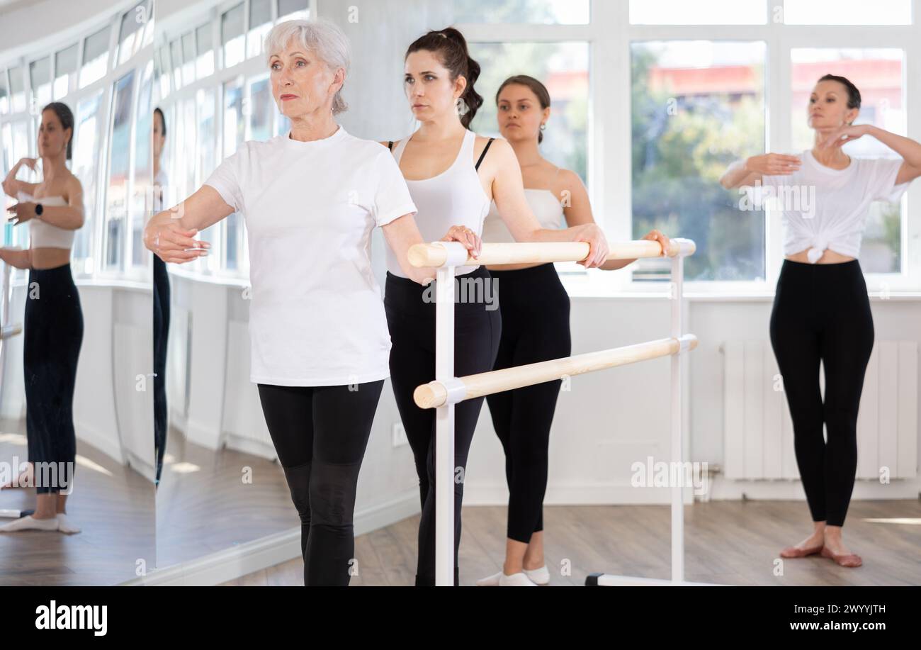 Elderly woman practicing ballet moves at barre during group class Stock Photo