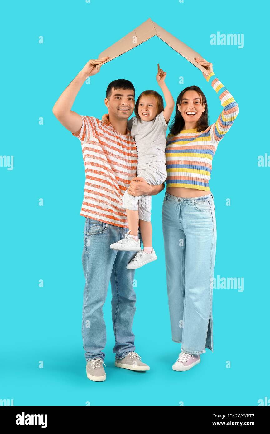 Happy family with cardboard in shape of roof dreaming about their new house on blue background Stock Photo