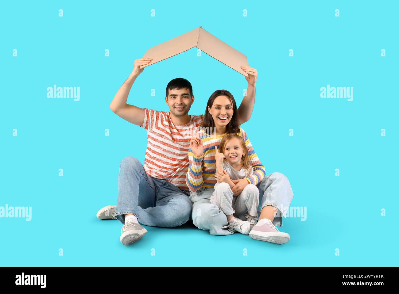 Happy family with cardboard in shape of roof dreaming about their new house on blue background Stock Photo