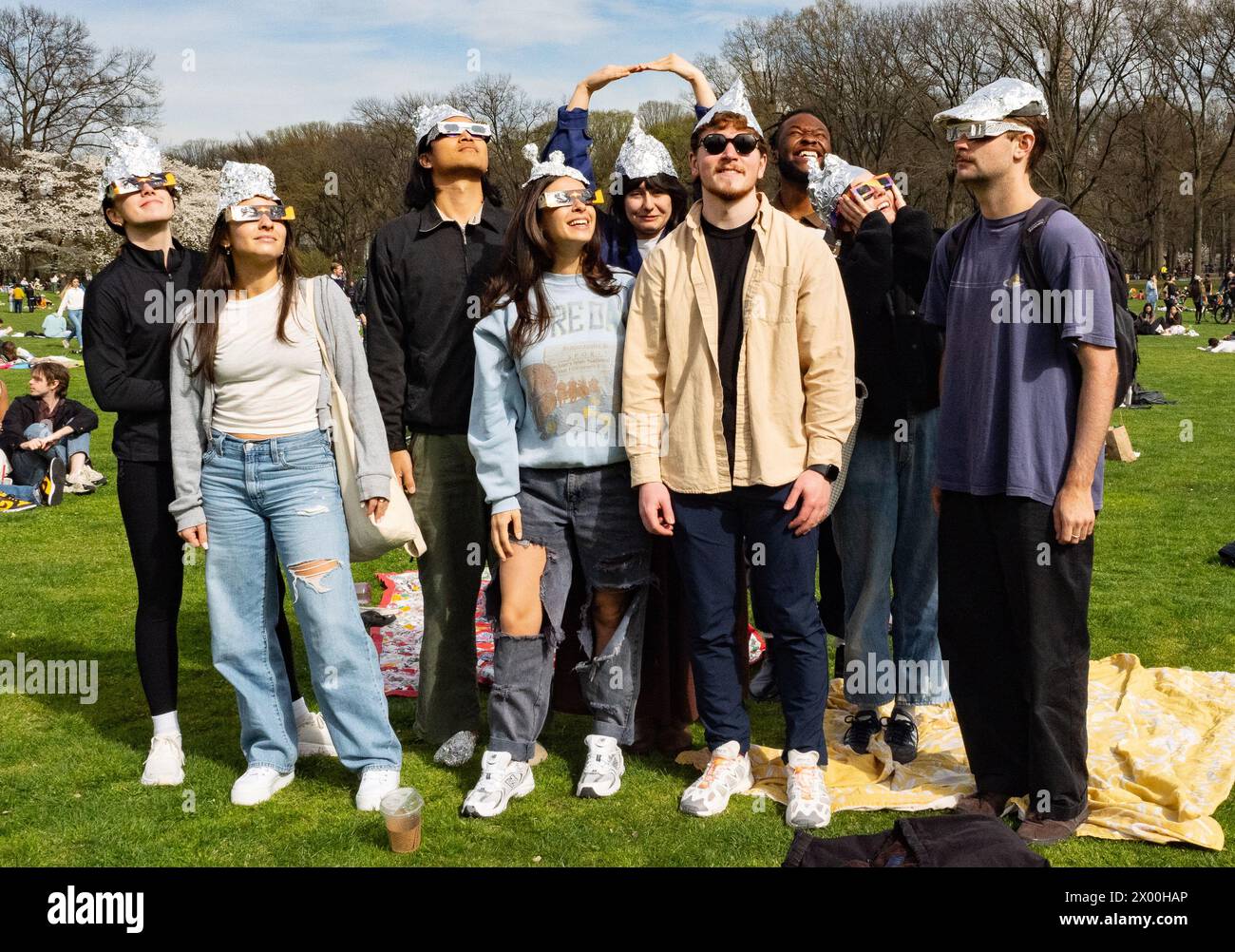 New York, New York, USA, April 8, 2024 Group of friends in tin foil hats amid the crowd gathered to watch the partial solar eclipse in Sheep's Meadow in New York City's Central Park on a beautiful spring day Stock Photo