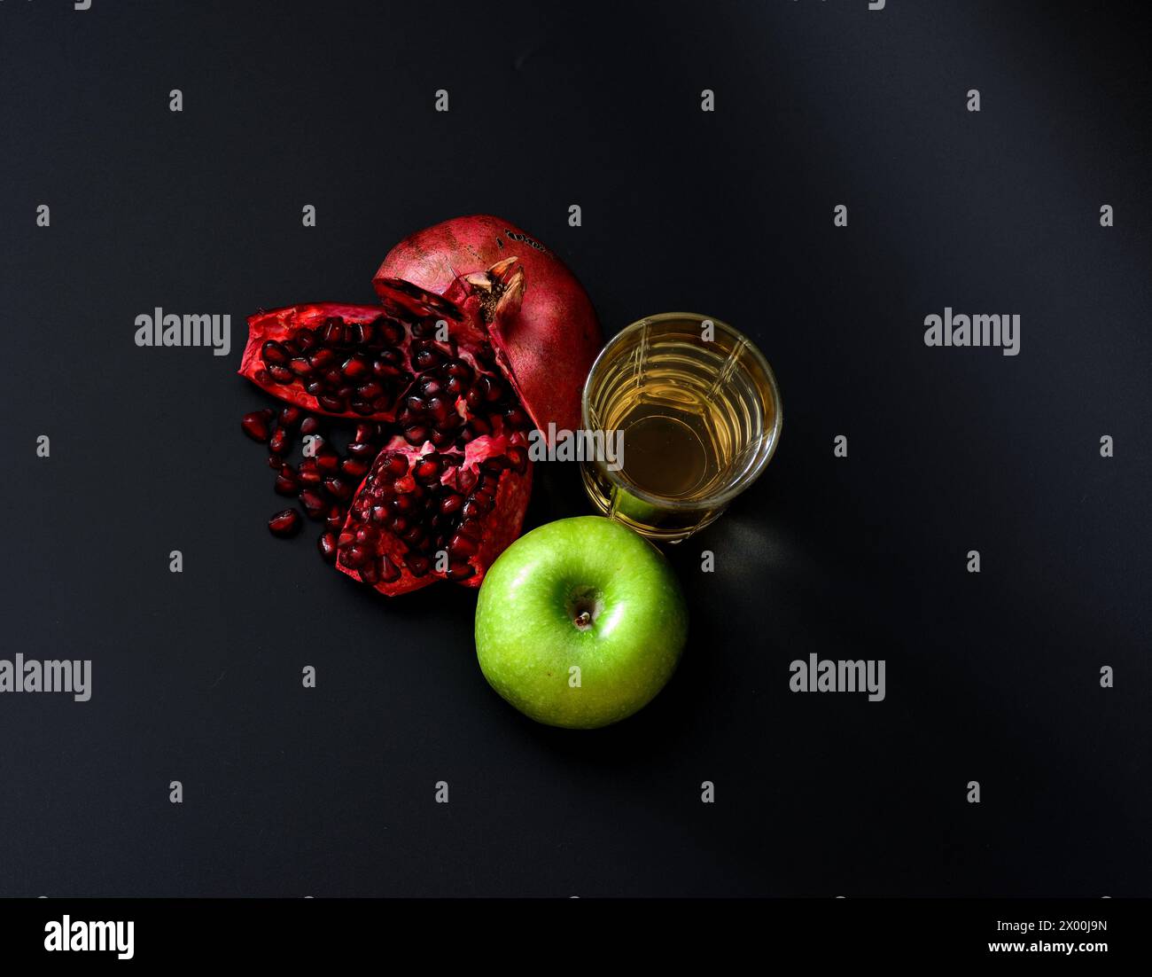 A tall glass of freshly squeezed fruit juice on a black background, next to a broken pomegranate fruit with seeds and a ripe green apple. Top view, fl Stock Photo