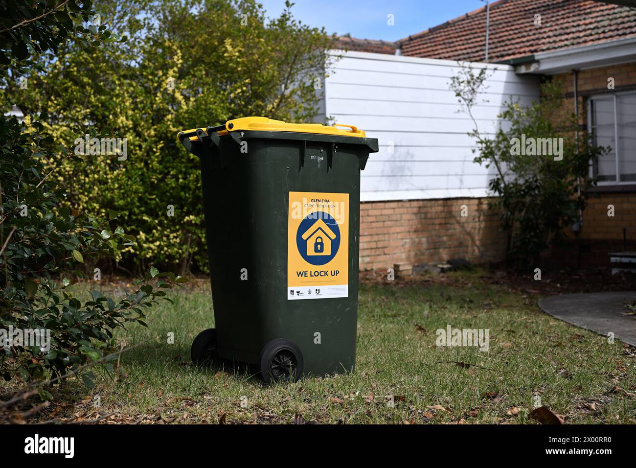 Yellow wheelie bin featuring Glen Eira crime prevention sticker with message, we lock up, part of the state government's living safely program Stock Photo