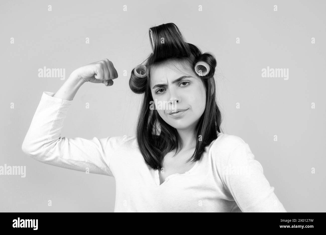 Woman with curlers. Funny housewife power. Pretty woman with curlers in her hair shows her strength and confidence. Stock Photo