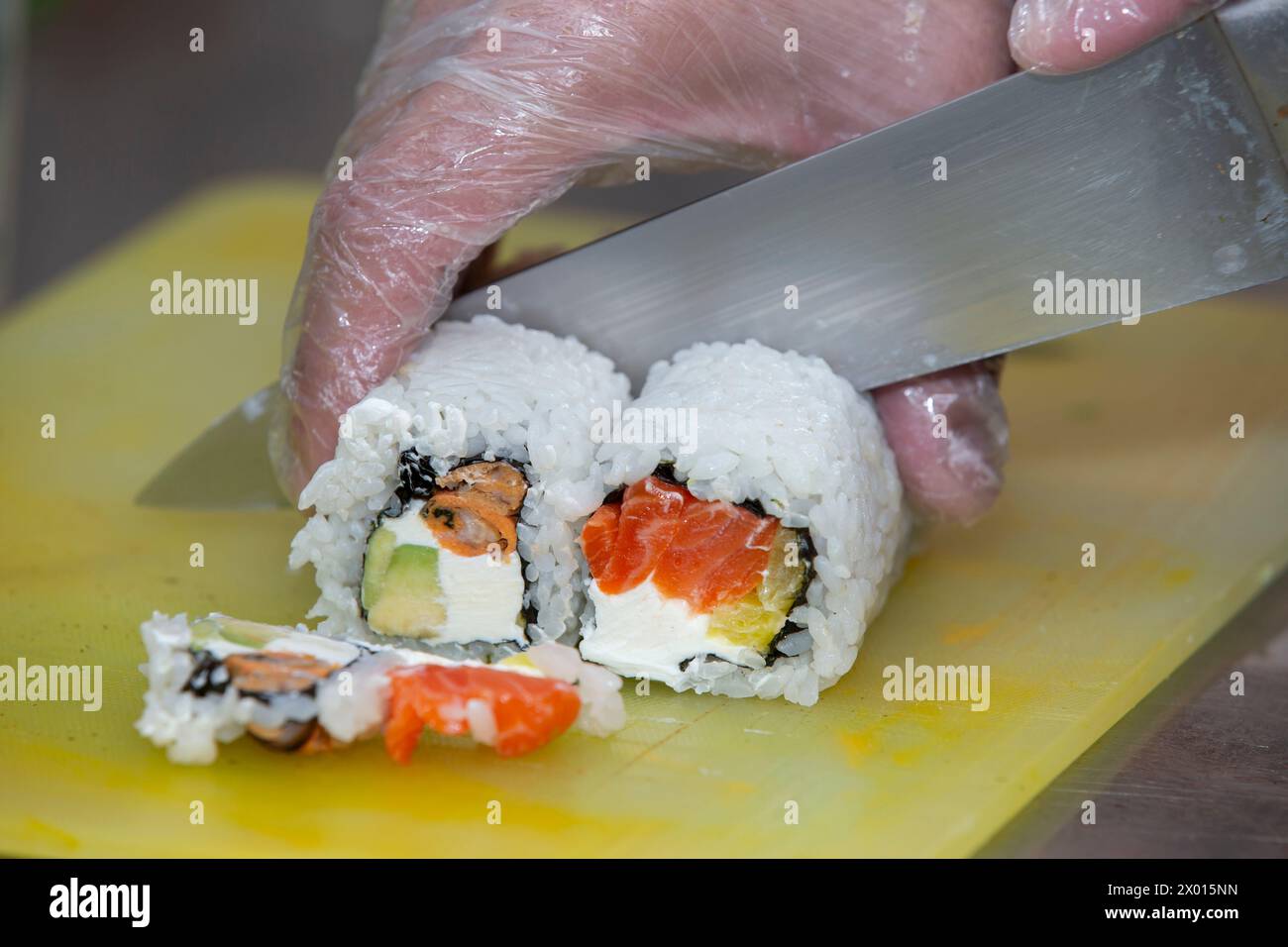 A gloved hand cuts sushi on a cutting board. Stock Photo