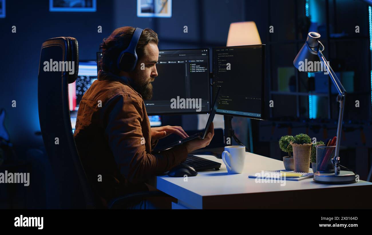 Developer focused on typing complex code in neon lit home office, listening music and developing software application. IT expert wearing headphones, solving coding project tasks on laptop, camera A Stock Photo