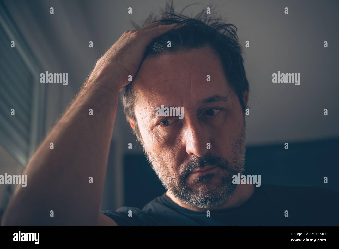 Disappointed adult caucasian male looking down in dark room, selective focus Stock Photo