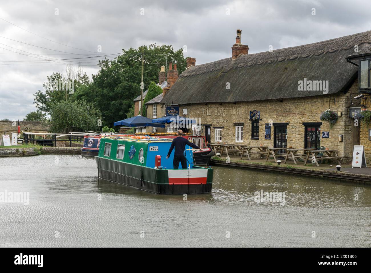 Narrowboat navigating the Grand Union canal with the Boat Inn in the background, Stoke Bruerne, Northamptonshire, UK Stock Photo