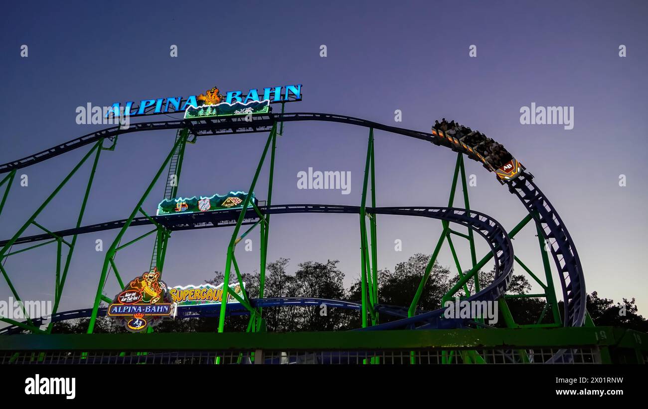 Herne, Germany - August.07.2023: Overview of the mobile roller coaster 'Alpina Bahn' at a funfair at night with illuminated train Stock Photo