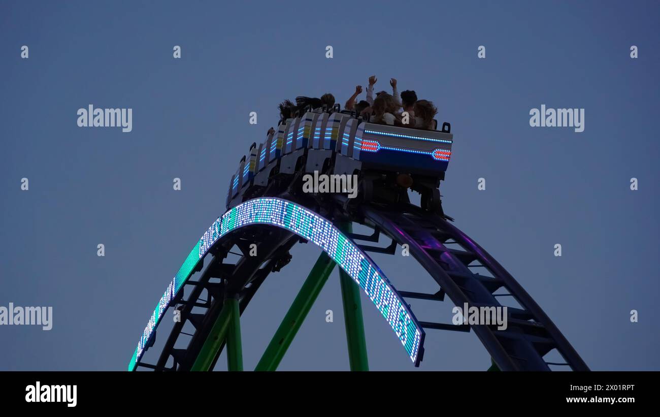 Herne, Germany - August.07.2023: Young people have fun in the illuminated train of the mobile roller coaster 'Alpina Bahn' at a funfair at night Stock Photo