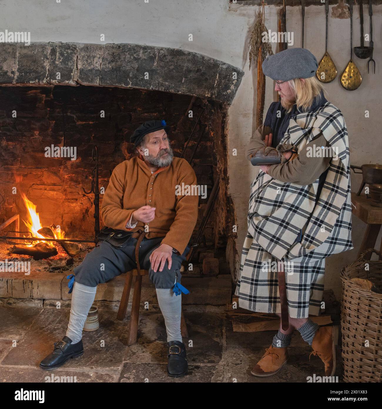 Two enactors dressed in period costume sat talking in the kitchens at Tretower Court and Castle, Tretower, Powys, Wales, UK. Stock Photo