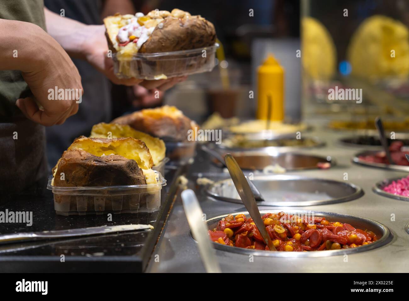 Turkish street food Kumpir. Male cook adds different fillings to the Kumpir. Delicious baked potatoes with a variety of mixed fillings Stock Photo