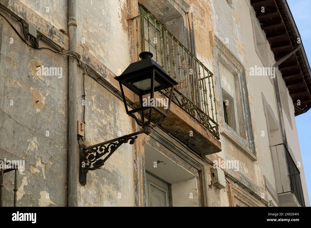 An old street lamp hangs from a building with peeling paint, highlighting the rustic charm of urban decay. Stock Photo