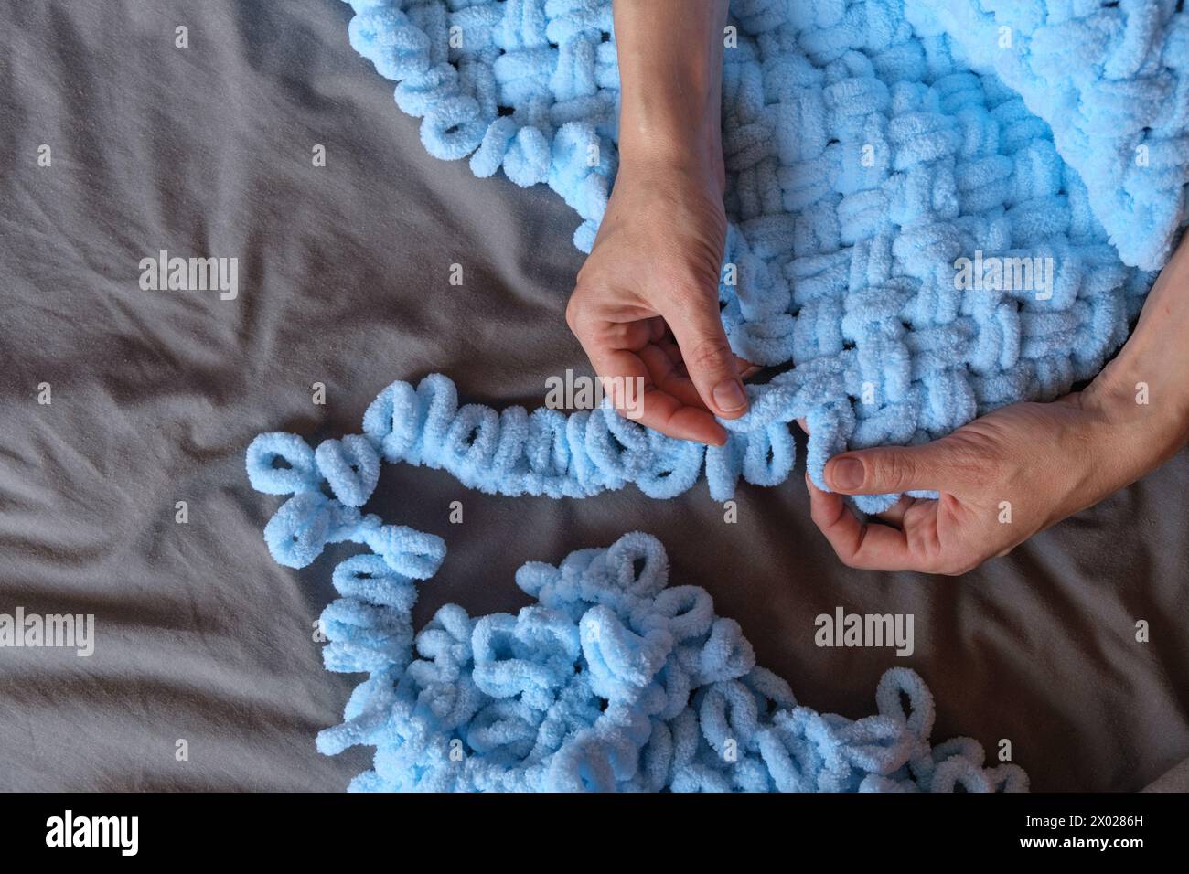 A woman lovingly crafts a blue blanket for her grandson with her own hands, each stitch a testament to her care and devotion. Create cherished memorie Stock Photo
