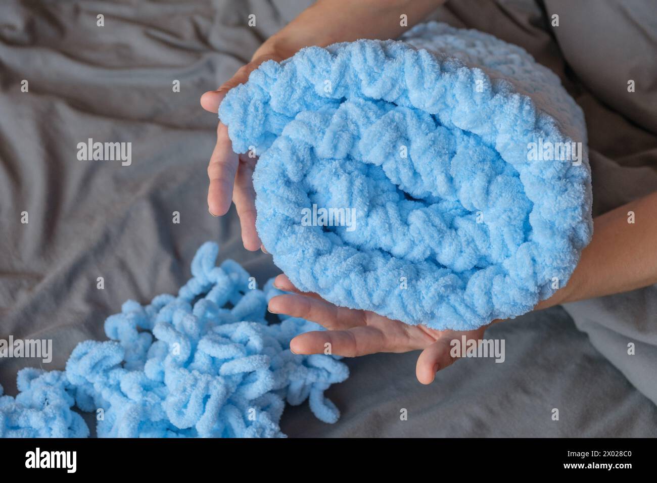 A woman lovingly crafts a blue blanket for her grandson with her own hands, each stitch a testament to her care and devotion. Create cherished memorie Stock Photo