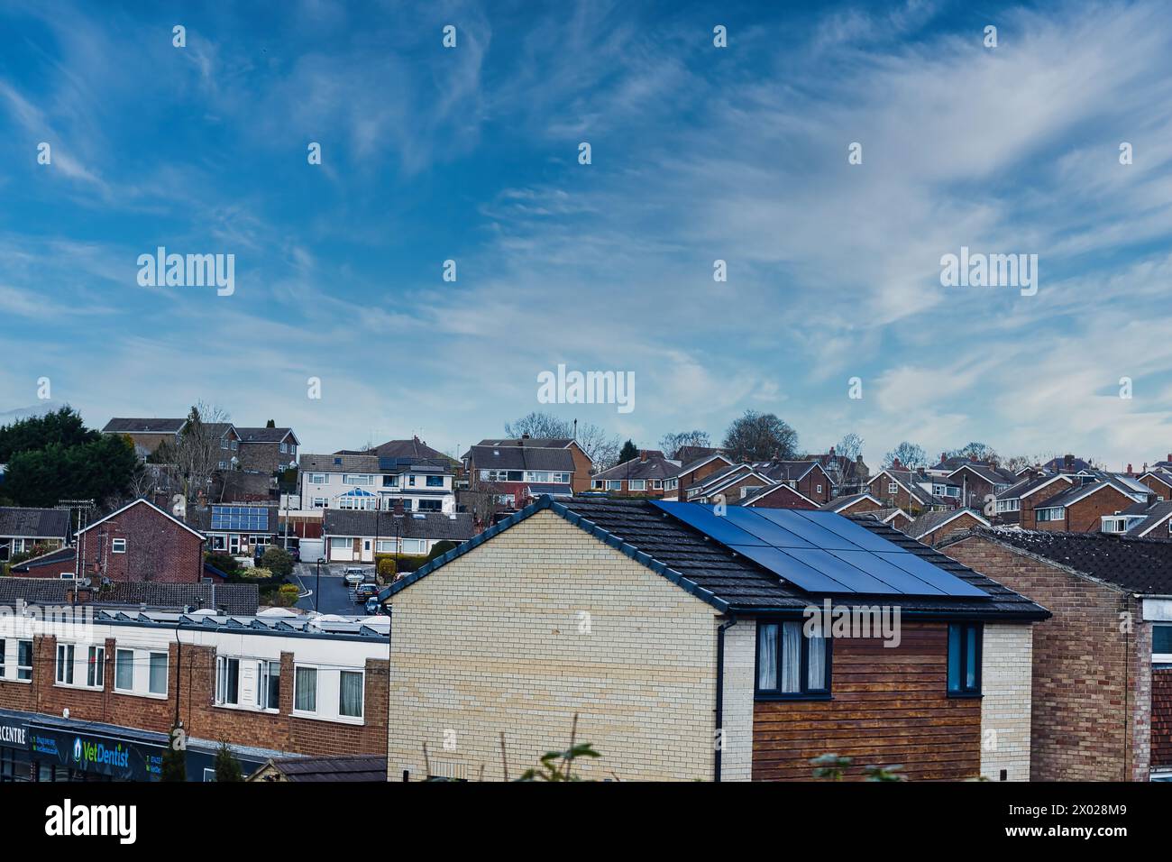 Suburban landscape with residential houses featuring solar panels under a dynamic blue sky with wispy clouds, showcasing sustainable living in a moder Stock Photo