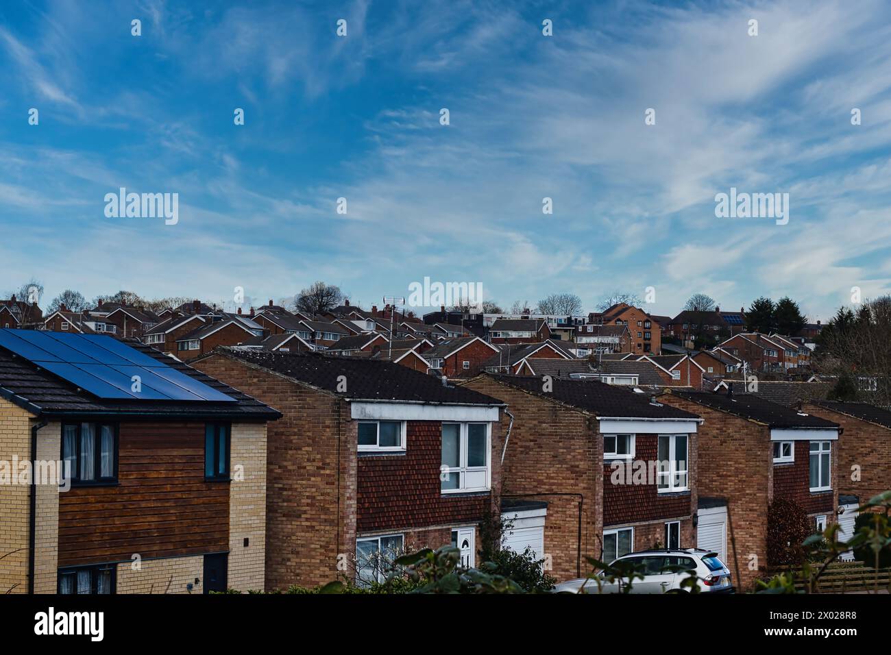 Suburban landscape with rows of British houses, featuring solar panels on roofs under a dynamic blue sky with wispy clouds in Harrogate, North Yorkshi Stock Photo