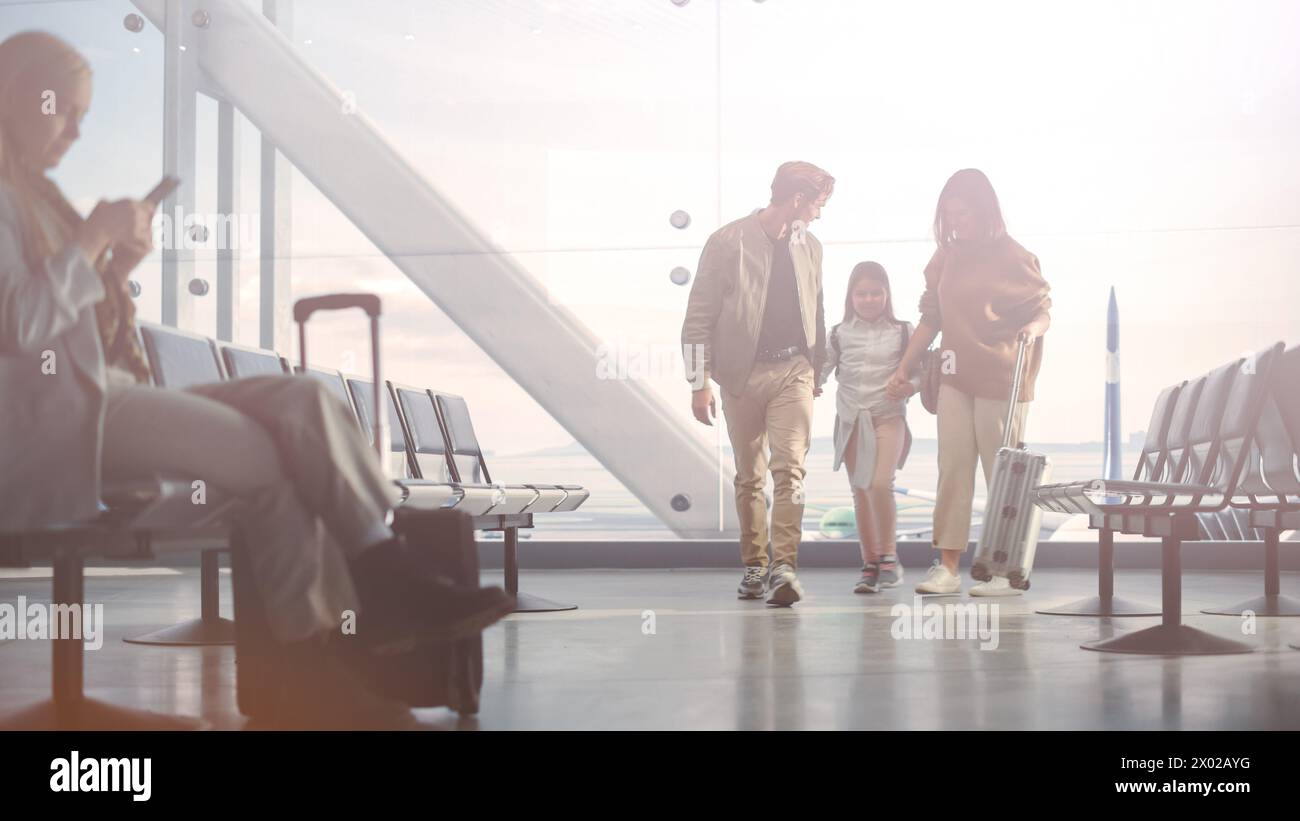 Airport Terminal Family Reunion: Caring Father Meets His Cute Little Daughter and Beautiful Wife at the Boarding Lounge of Airline Hub. He Picks Up and Dances with Lovely Child and Hugs His Partner Stock Photo