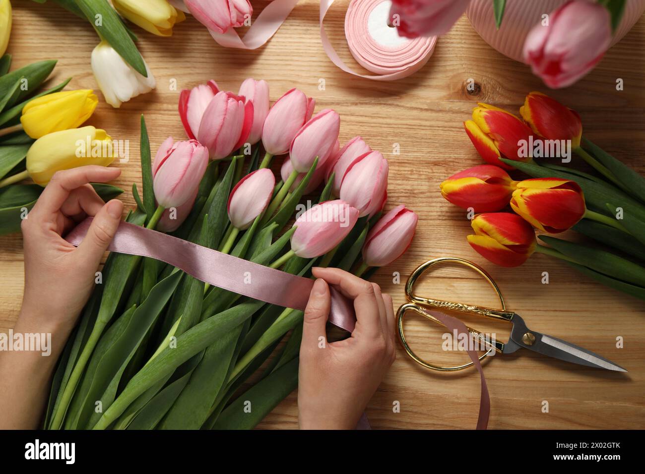 Woman making beautiful bouquet of fresh tulips and ribbon at wooden ...