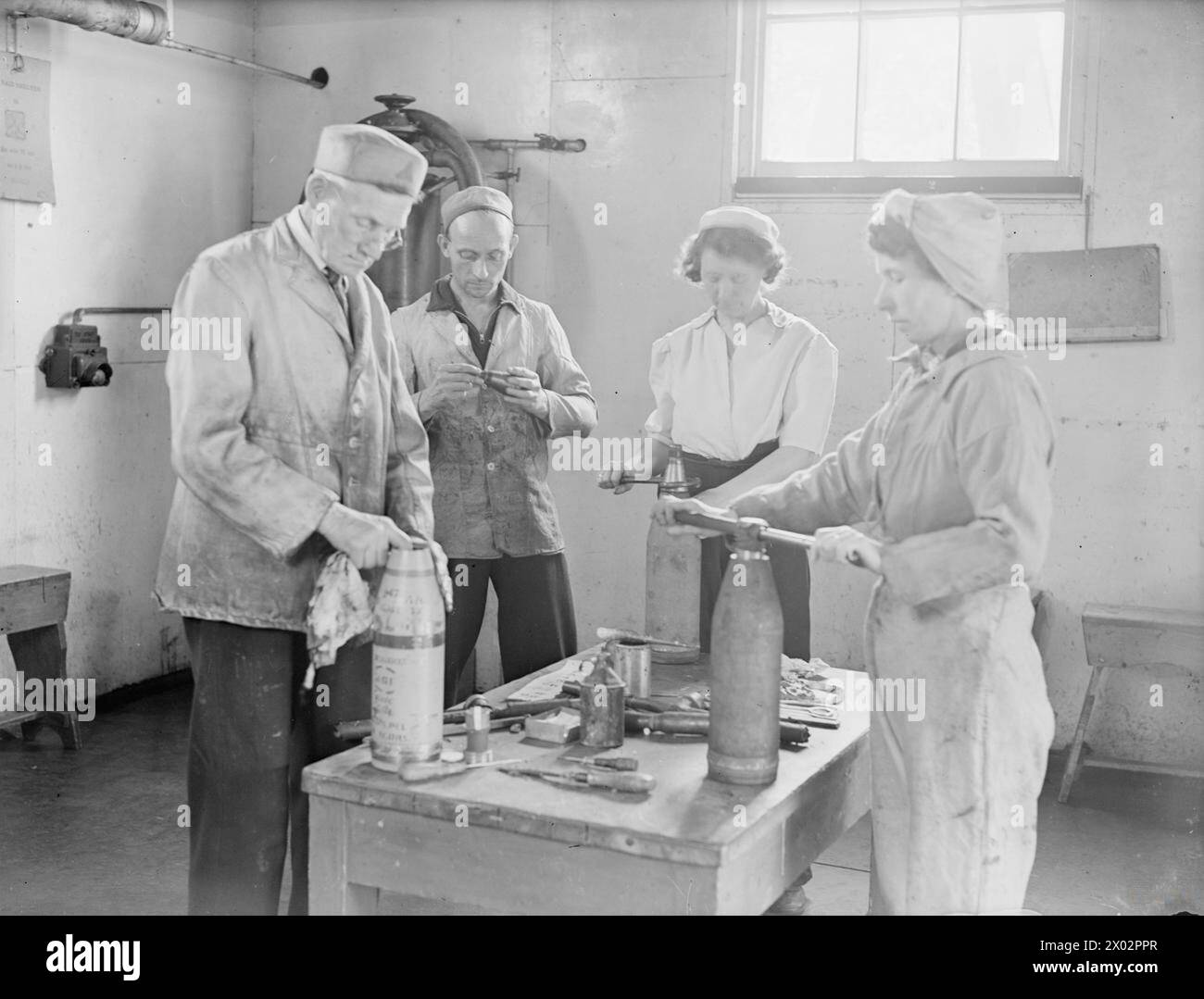 MEN AND WOMEN BEHIND THE GUNS OF THE BRITISH NAVY. 25 TO 30 JULY 1944, AT VARIOUS ARMAMENT DEPOTS AND FACTORIES IN THE SOUTH OF ENGLAND (PRIDDY'S HARD, DEAN'S HILL, MILTON HEATH, AND BATH). SOME OF THE EMPLOYEES OF THE ARMAMENT SUPPLY DEPARTMENT OF THE ADMIRALTY. - Defusing shells from a damaged destroyer. Left to right: William Tillman; Ernest Goff, Chargehand, who has been in the department for 28 years; Mrs Margaret Bristow, wife of a Royal Marine; and Mrs Amy Harding, wife of an Able Seaman in the NELSON  Tillman, William Thomas, Goff, Ernest F Stock Photo