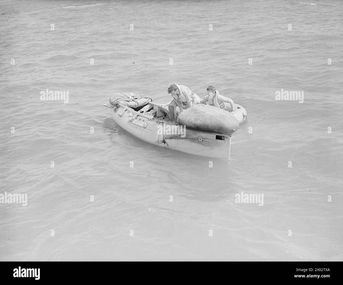 LIFEBOAT DROPPED FROM AIR. 13 JULY 1945, LEE-ON-SOLENT. THE DEMONSTRATION DROP OF THE NAVY'S AIRBORNE LIFEBOAT, 17 FT, 9 INS LONG, WHEN IT WAS DROPPED BY PARACHUTE TO AN AIR CREW WHO WERE SUPPOSED TO HAVE FORCED LANDED INTO THE SEA. THE LIFEBOAT, SELF-RIGHTING, AND SELF-BALING IS EQUIPPED WITH SAILS AND AN OUTBOARD ENGINE WHICH GIVES IT A RANGE OF 120 MILES AT 4 KNOTS. - 'Air crew' clambering into the lifeboat Stock Photo