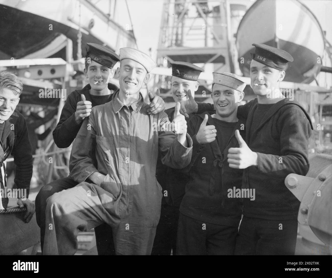 ARRIVAL OF THE FIRST FLOTILLA OF AMERICAN DESTROYERS FOR ROYAL NAVY. 28 SEPTEMBER 1940, ROYAL DOCKYARD, DEVONPORT. THE FLOTILLA, HANDED OVER BY THE US GOVERNMENT UNDER THE AGREEMENT, WERE MANNED ENTIRELY BY BRITISH CREWS. - "Thumbs Up" by members of the British naval crew who brought the destroyers to this country. Two of the crew brought American Naval caps which they obtained from the destroyer's American crew who were on board prior to the handing over Stock Photo