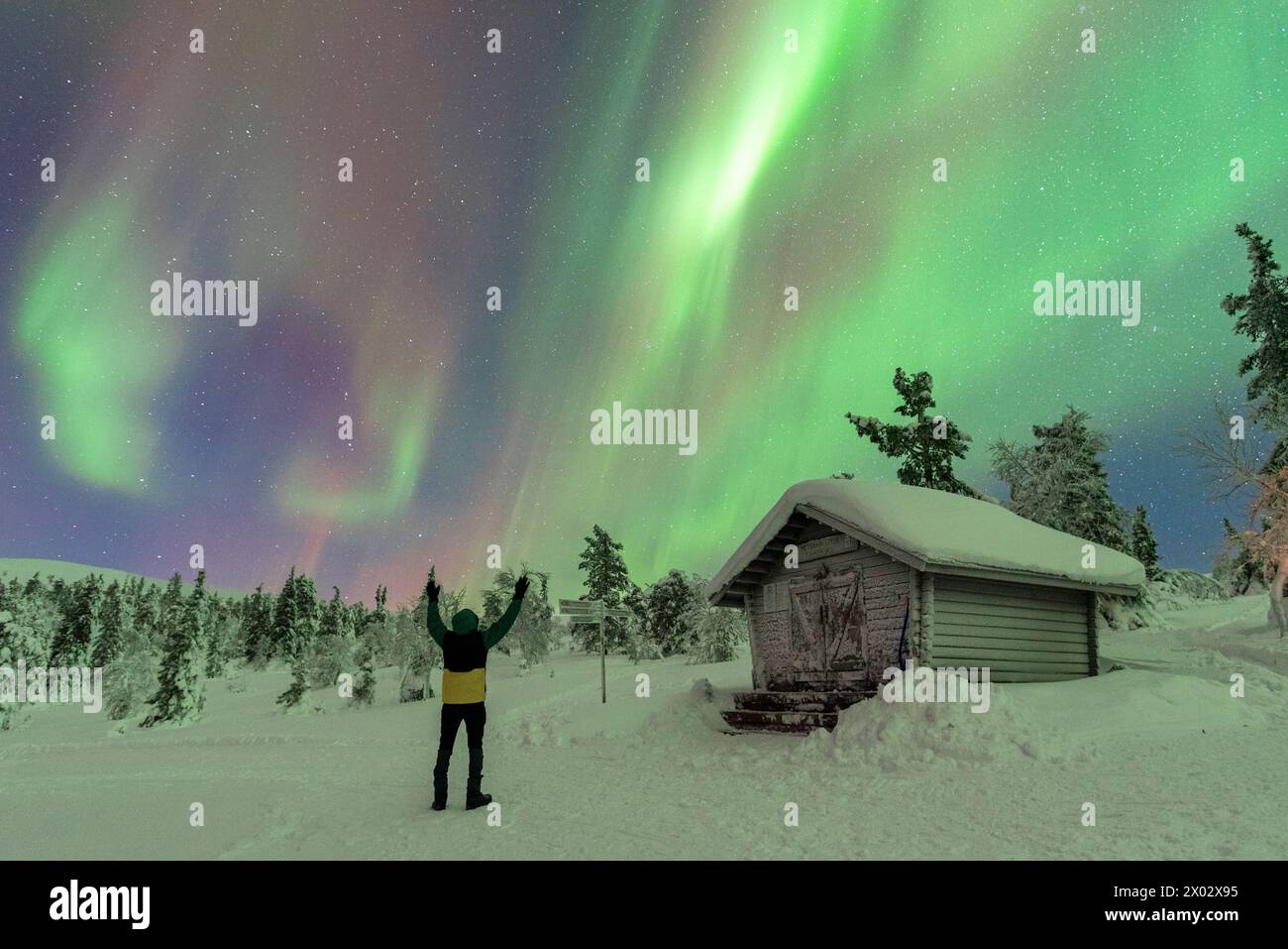 Happy tourist waving at the Northern Lights (Aurora Borealis) dancing in the night sky above the Arctic Circle, Akaslompolo, Kolari municipality Stock Photo