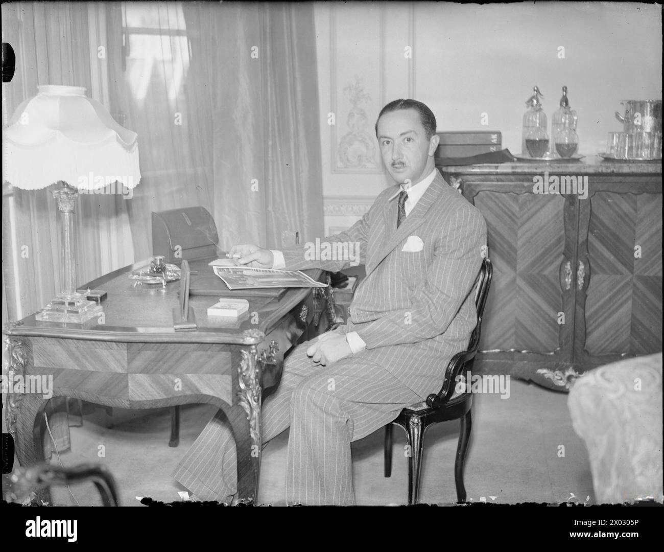 HIS ROYAL HIGHNESS THE EMIR ABDUL ILLAH, REGENT OF IRAQ, LONDON, ENGLAND, UK, JULY 1945 - A portrait of the Regent of Iraq sitting at his desk in his room at Claridge's Hotel in London. According to the original caption, the Regent spent July in England on his way back to Iraq following the San Francisco conference. He is looking at a group photograph, possibly taken at the Conference  Abdul-Illah, Emir of Iraq Stock Photo