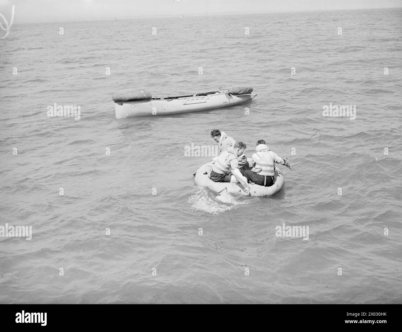 LIFEBOAT DROPPED FROM AIR. 13 JULY 1945, LEE-ON-SOLENT. THE DEMONSTRATION DROP OF THE NAVY'S AIRBORNE LIFEBOAT, 17 FT, 9 INS LONG, WHEN IT WAS DROPPED BY PARACHUTE TO AN AIR CREW WHO WERE SUPPOSED TO HAVE FORCED LANDED INTO THE SEA. THE LIFEBOAT, SELF-RIGHTING, AND SELF-BALING IS EQUIPPED WITH SAILS AND AN OUTBOARD ENGINE WHICH GIVES IT A RANGE OF 120 MILES AT 4 KNOTS. - 'Ditched air crew' in dinghy paddle towards the lifeboat as it touches down Stock Photo