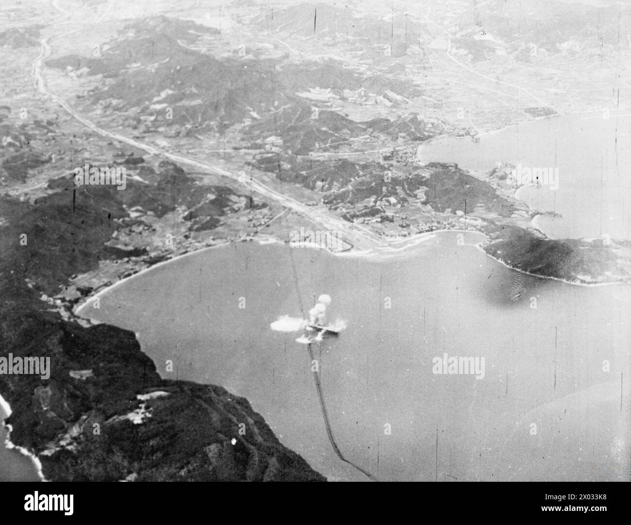 JAPANESE CARRIER IN INLAND SEA HIT BY BRITISH NAVY BOMBS. 24 JULY 1945, AERIAL PHOTOGRAPHS FROM AN ATTACKING AIRCRAFT OF THE BRITISH PACIFIC FLEET. - British Naval aircraft of the British Pacific Fleet Task Force score a direct hit on a Japanese escort carrier of the Kobe class in Shido Wan, a bay on the coast of Shikoku. The carrier, the SHIMANE MARU, was wrecked by a bomb going down the aircraft well Stock Photo
