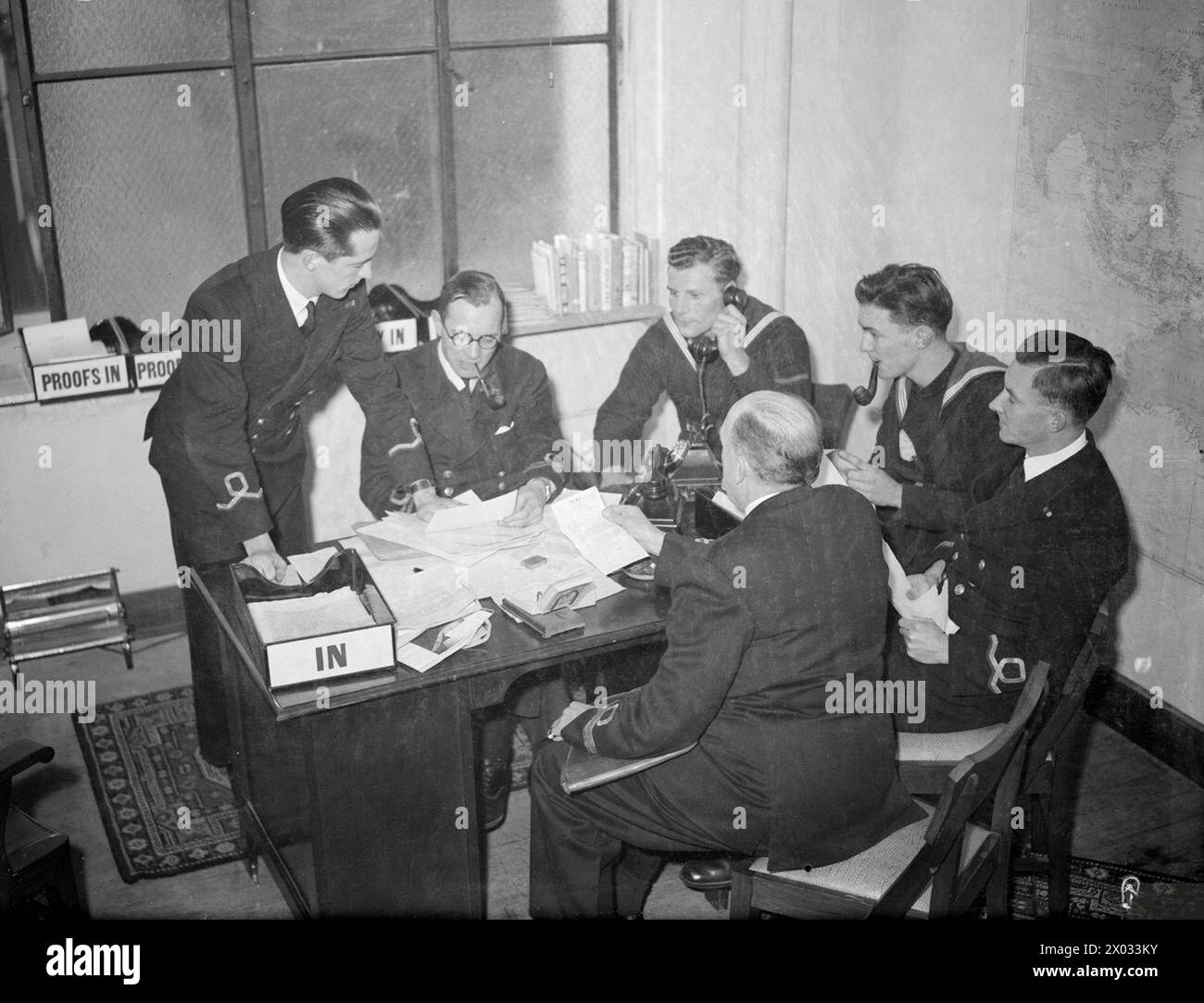 BRITISH PACIFIC FLEET'S NEWSPAPER. AUGUST 1945, SYDNEY, AUSTRALIA. PRODUCTION AND DISTRIBUTION OF THE BRITISH PACIFIC FLEET'S OWN NEWSPAPER, 'PACIFIC POST', BY THE NAVY, FOR THE NAVY. - The editorial conference held each morning to discuss policy and layout. Left to right: Sub Lieut E P Glover, RNVR, of Blackburn, Lancs, Sports Editor; Lieut John Willis, RNVR, of Snaresbrook, Essex, Editor and former Fleet Street journalist; Signalman R Hatchett of London; O/S F W Guy of Spalding; Sub Lieut D J Newton, RNVR; and Lieut A H Bowley, RNVR Stock Photo