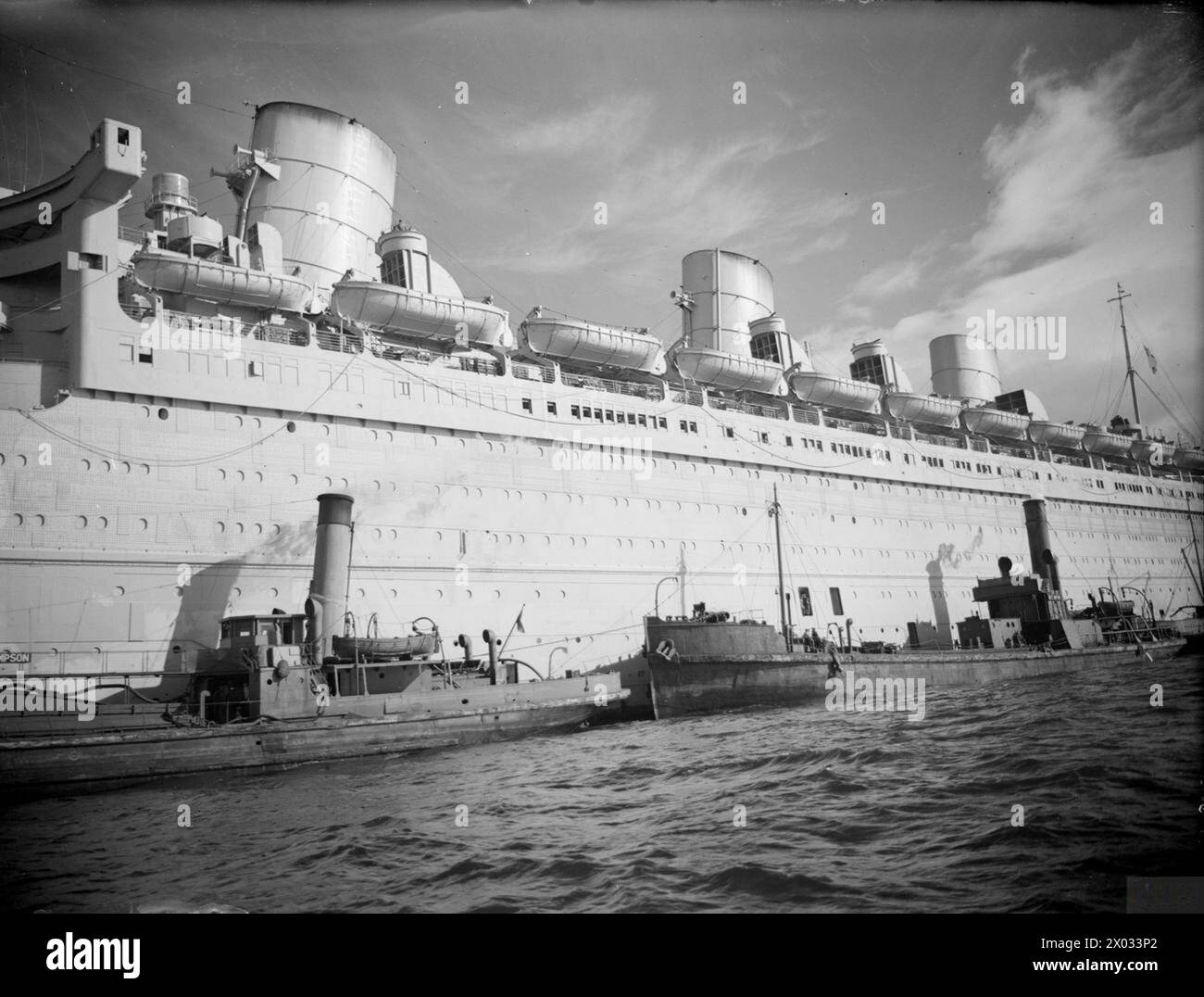 THE QUEEN MARY ON WAR SERVICE. 28 SEPTEMBER 1944, GREENOCK. THE 84000 TON CUNARD LINER QUEEN MARY IN HER GREY WHITE WAR PAINT AS SHE PREPARED TO MAKE ANOTHER ATLANTIC CROSSING TAKING WOUNDED US TROOPS BACK TO AMERICA. - In her war paint with attendant harbour vessels alongside Stock Photo