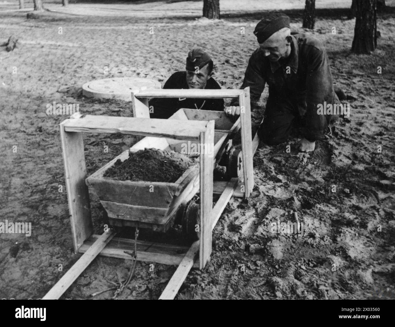 THE GREAT ESCAPE, MARCH 1944 - They put it on rails in two of the shoving frames which they re-assembled upside down - the box frames were narrower at the top. Corporal Karl Greise, one of the German guards known as 'Rubberneck', and Sergeant-Major Hermann Glemnitz, the senior member of the German guard, demonstrating a cart used for removing earth from the 'Harry' escape tunnel at Stalag Luft III, Sagan. Photograph probably taken in late March 1944  German Air Force, Glemnitz, Hermann, Greise, Karl Stock Photo