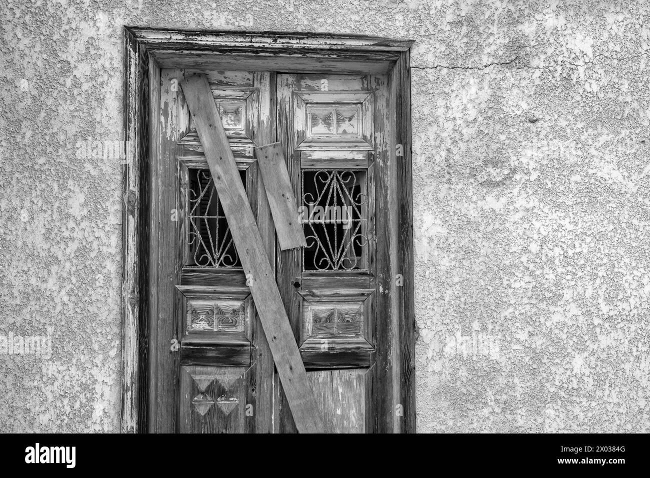 A black and white image of planks covering a boarded up door on a derelict arabian house in the middle east. Stock Photo
