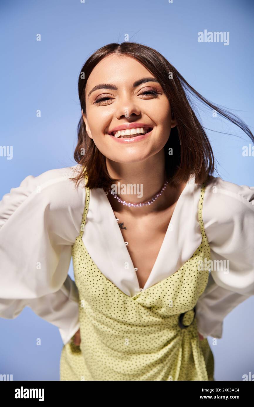 A joyful young woman with brunette hair smiles brightly at the camera, dressed in a vibrant yellow outfit. Stock Photo