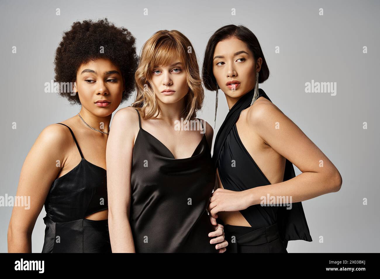 Three women in black dresses strike a pose for a picture against a grey ...