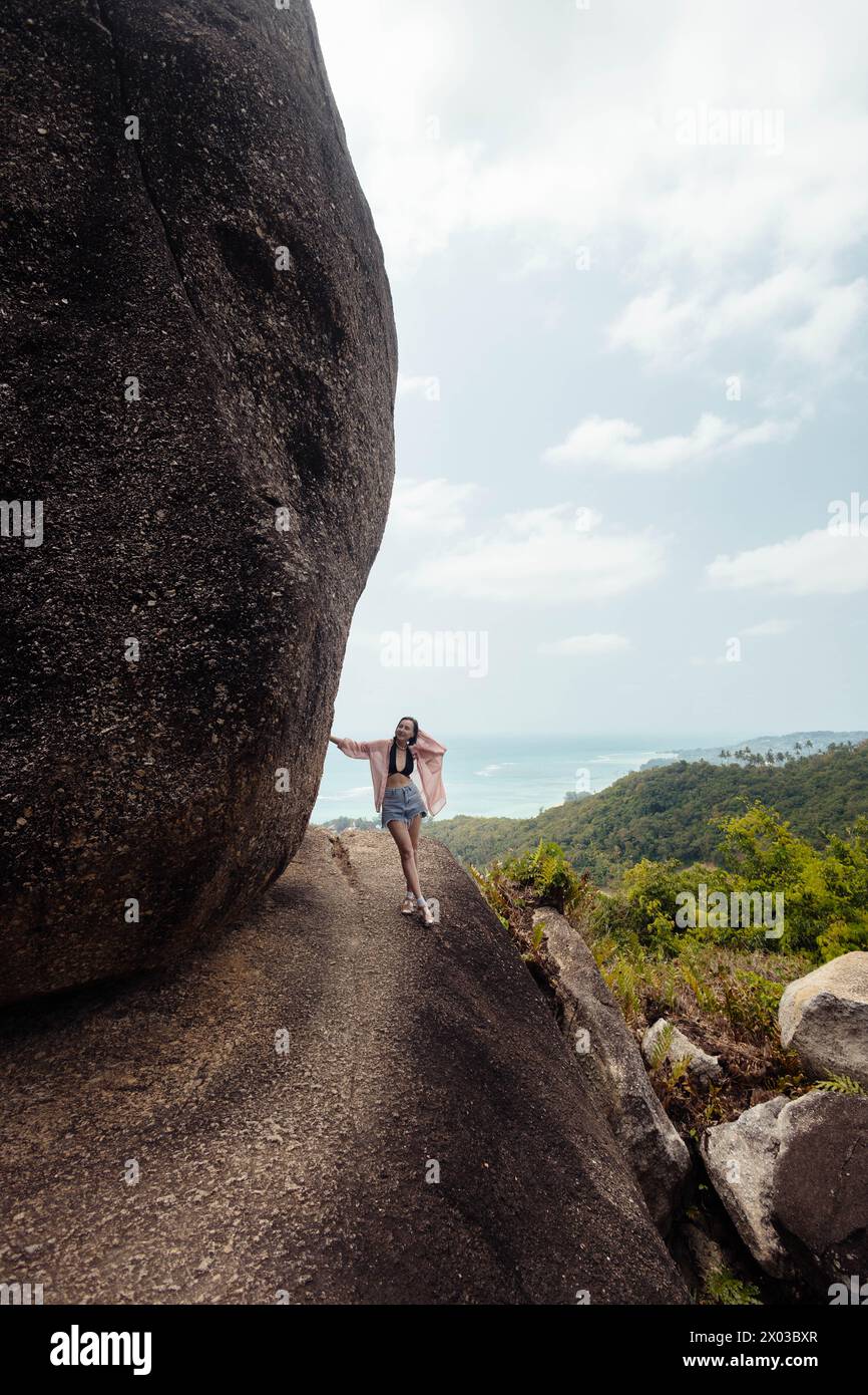 Woman stands confidently on a massive rock formation, overlooking the landscape below Stock Photo