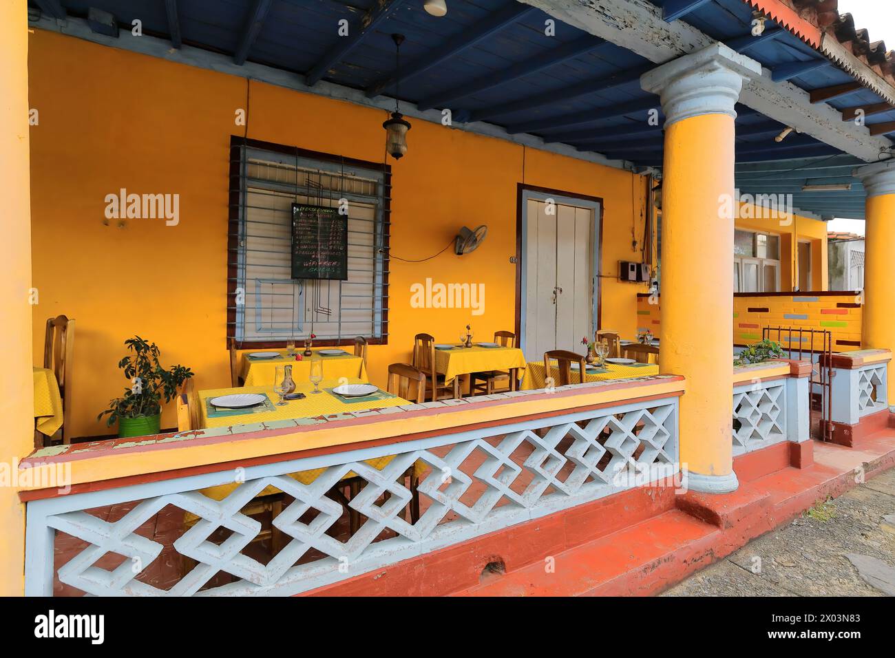 153 Restaurant porch with walls painted yellow-orange and blue wood ceiling hosting small tables on Calle Salvador Cisneros Street. Viñales-Cuba. Stock Photo