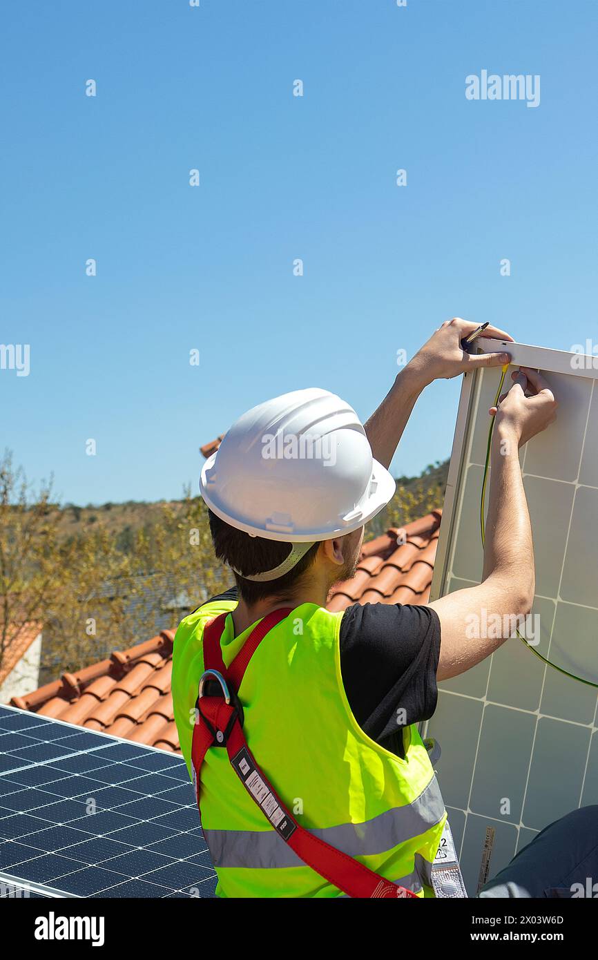 Man technician mounting photovoltaic solar moduls on roof of house. Engineer in helmet installing solar panel system outdoors. Concept of alternative and renewable energy. High quality photo Stock Photo
