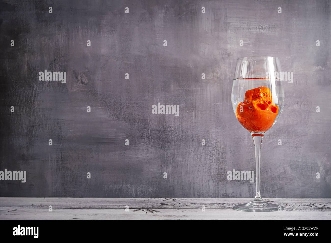 An upside down orange skull trying to drown in a glass of water Stock