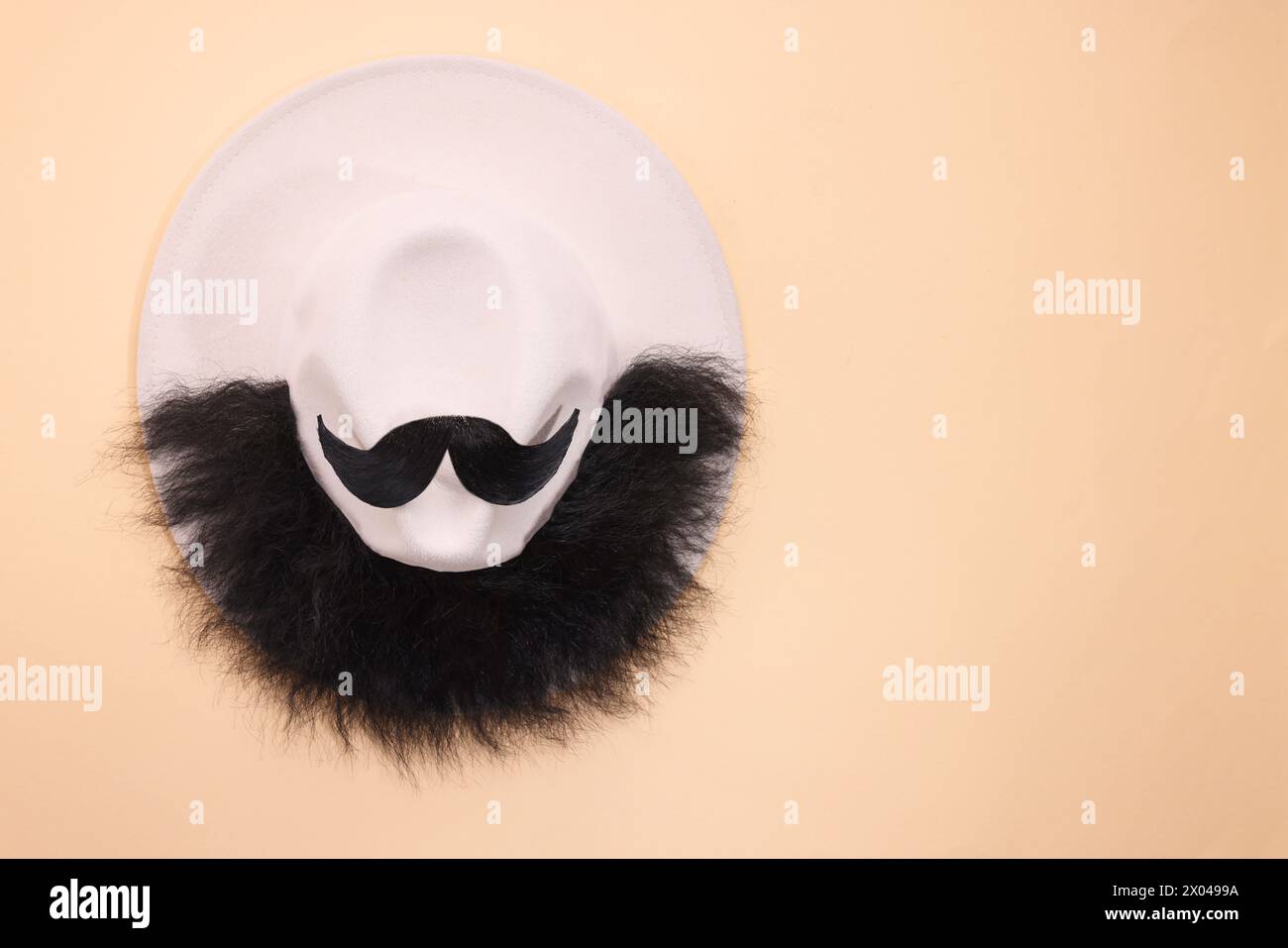 Man's face made of artificial mustache, beard and hat on beige background, top view. Space for text Stock Photo
